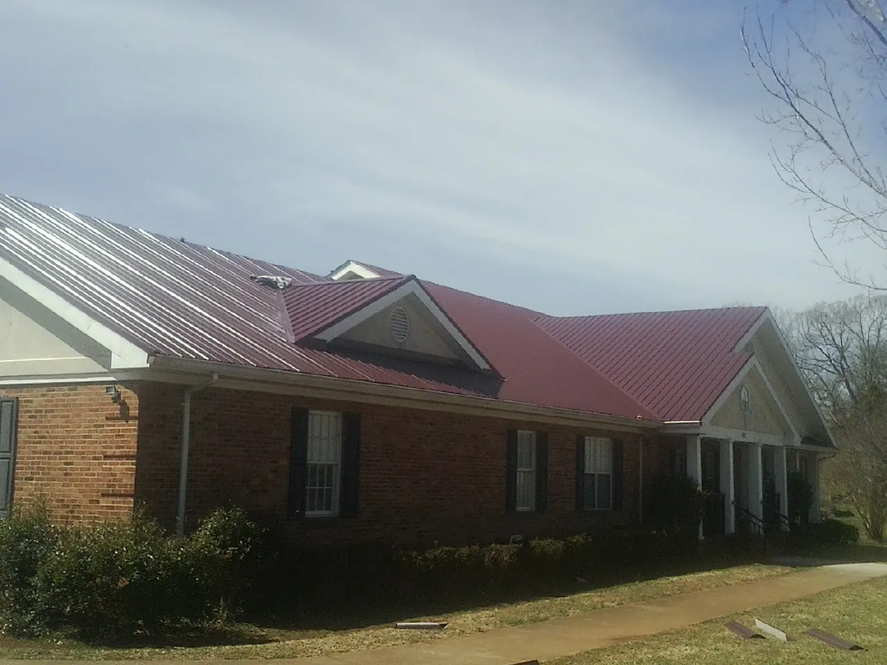 Red metal roof with gabled entries on a long brick building, from a Hail Damage Roof Repair job in Spring Lake