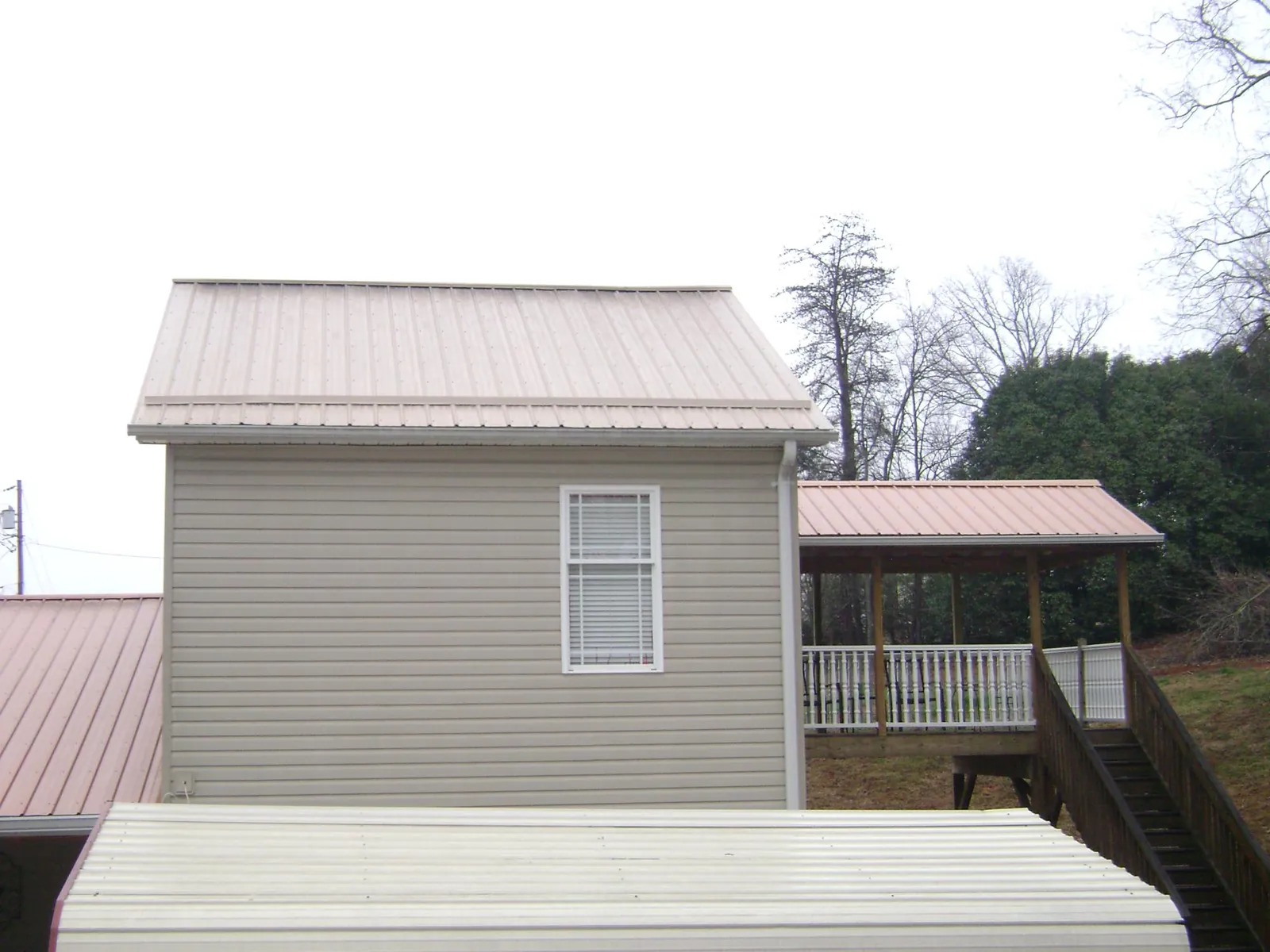 Tan metal roofs on a two story addition and attached porch, from a Roof Replacement job in Spring Lake